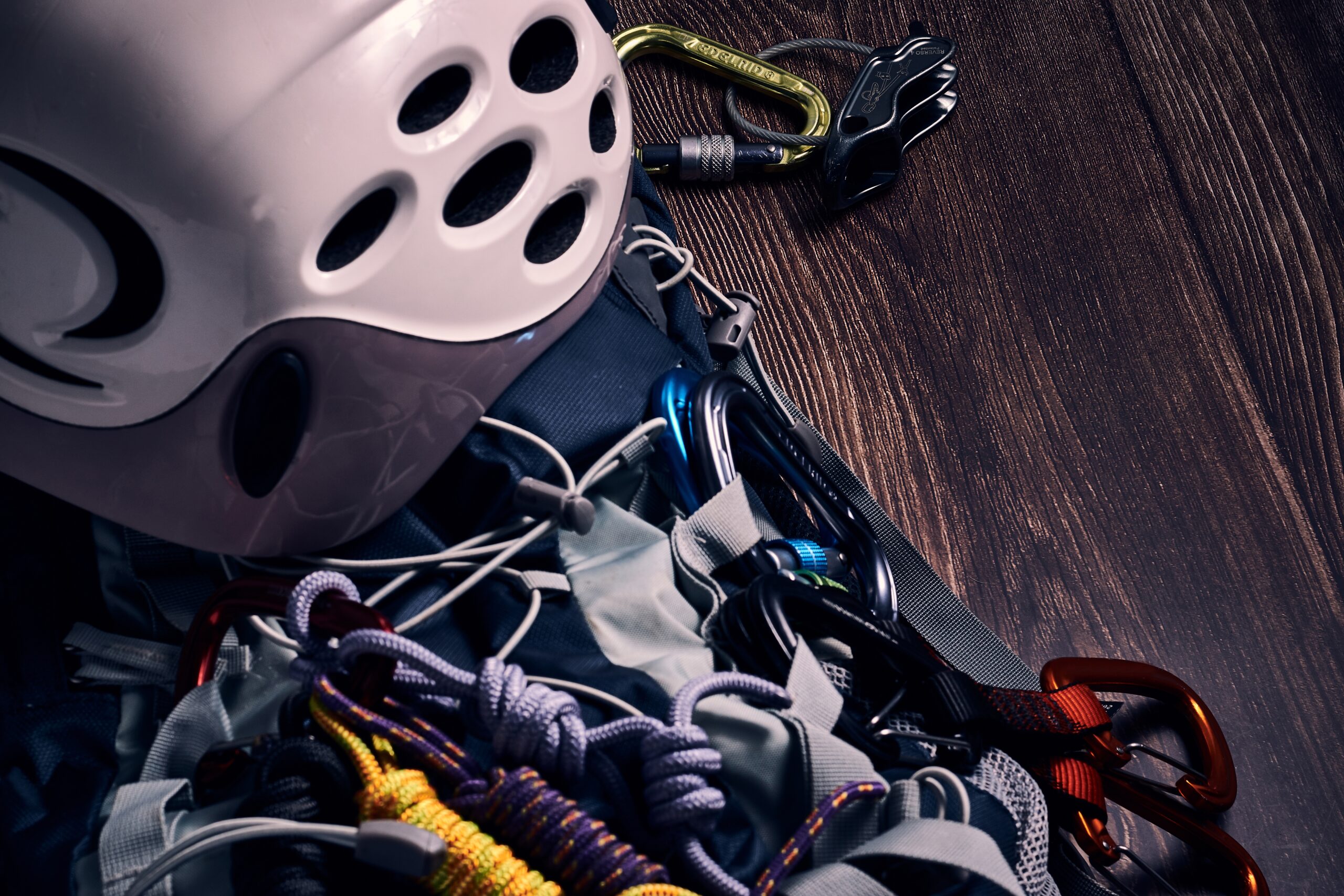 A collection of rappelling equipment, including a rope, harness, carabiners, rappel device, gloves, and helmet, laid out neatly on a flat surface.
