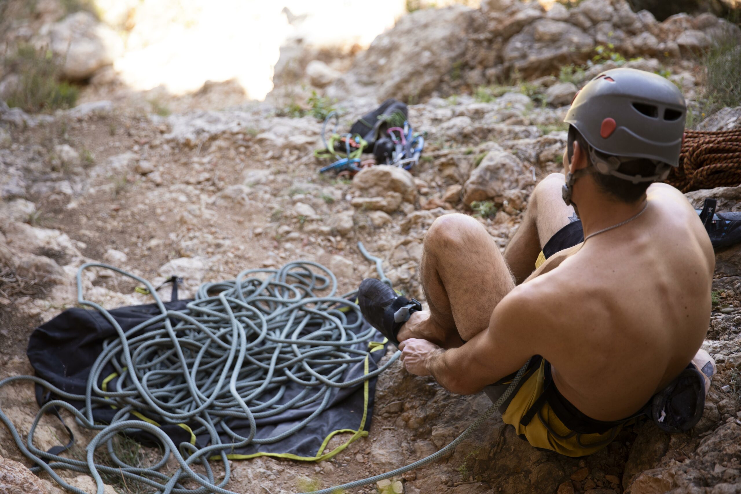 An overhead view of a person wearing a helmet and harness and carrying a coiled rope over their shoulder while hiking to a rappelling location.