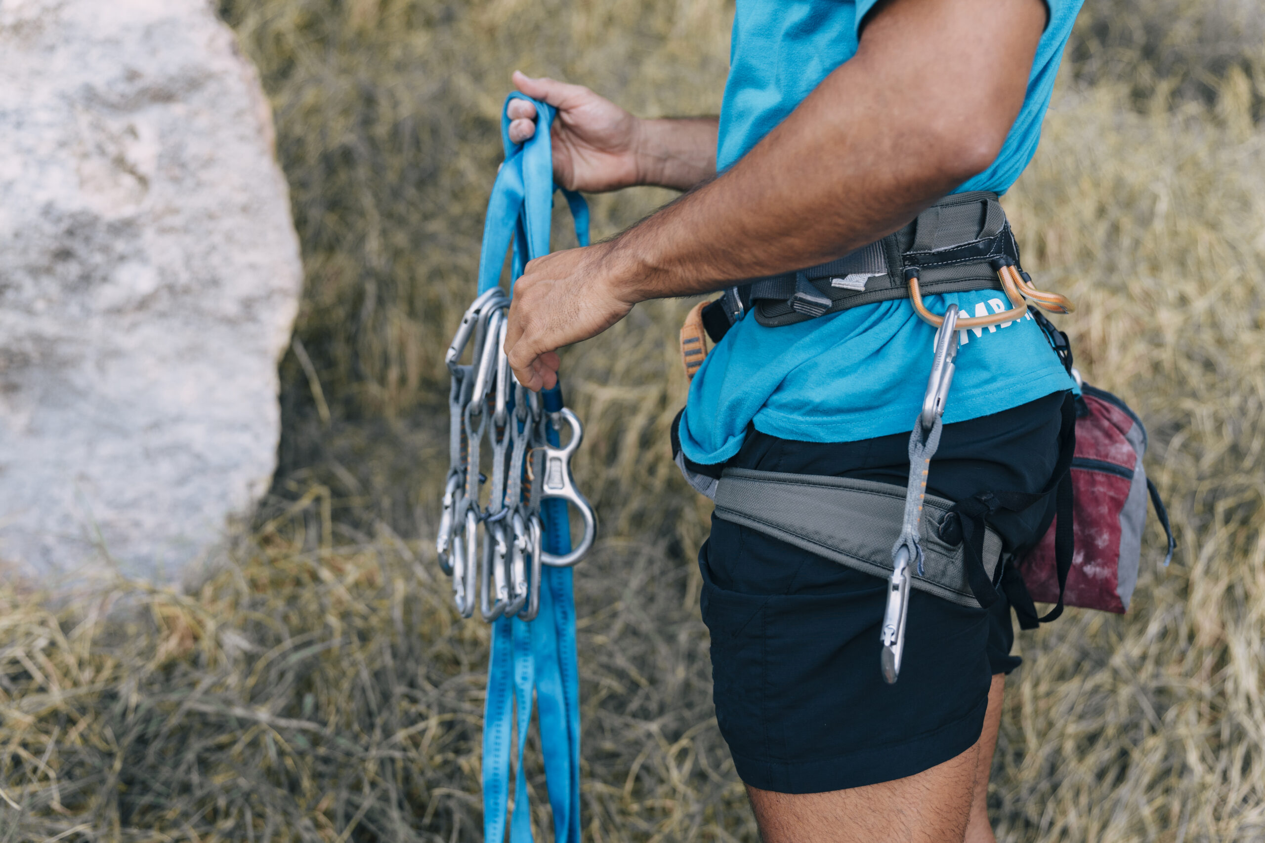 A close-up of a person's hands checking their rappelling equipment, including the rope, harness, carabiners, and rappel device, to ensure they are secure and functioning correctly.